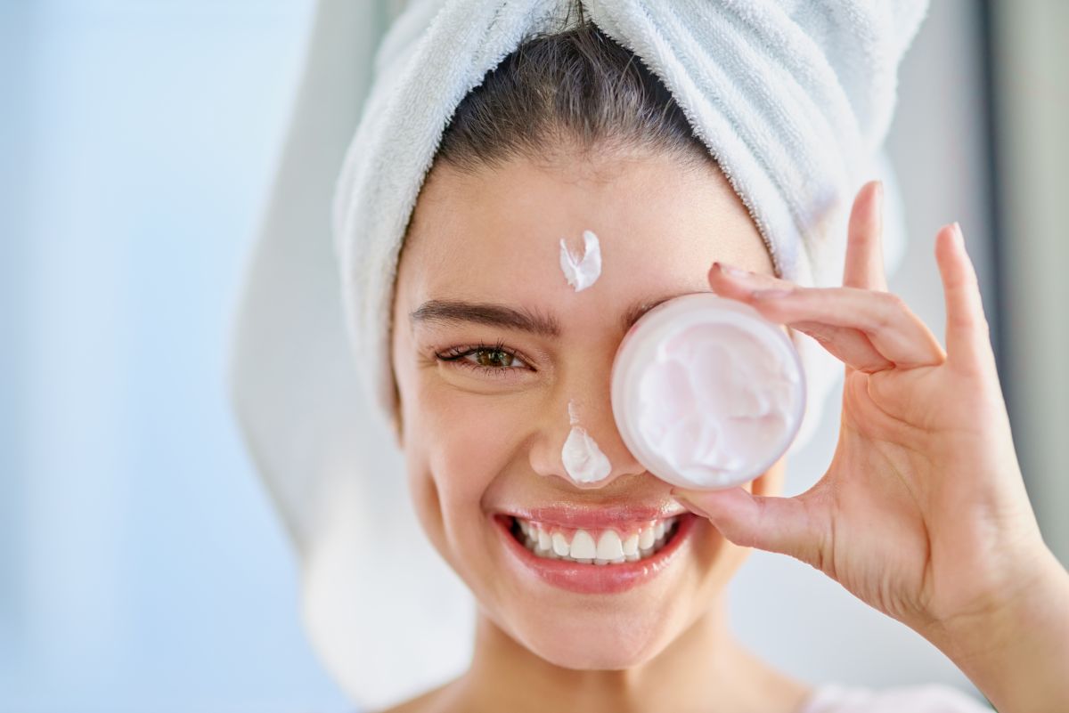 Woman applying moisturizer in winter setting, showing glowing, hydrated skin with winter skincare products from Natural Beauty Spa.